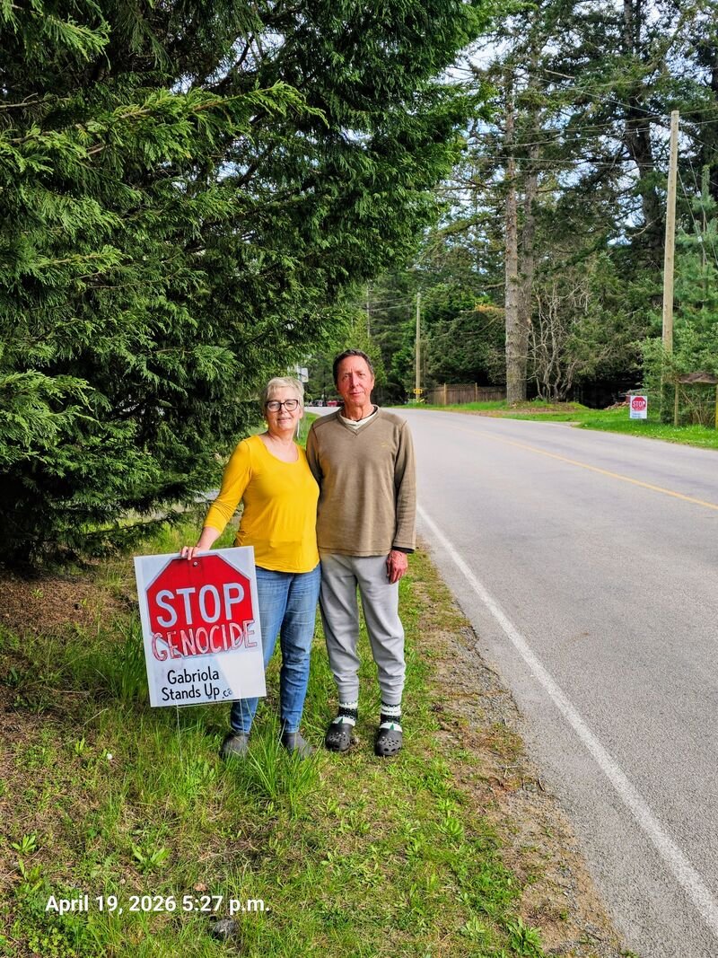 Connie and Paul with their Stop Genocide sign on South Road, Gabriola — three signs visible