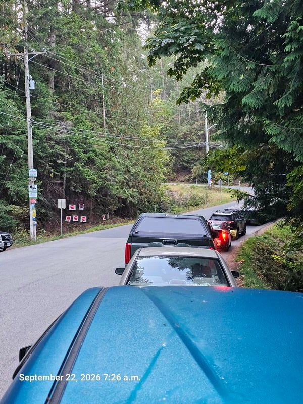 Cars lined up for the ferry passing STOP GENOCIDE signs on Taylor Bay Road, Gabriola